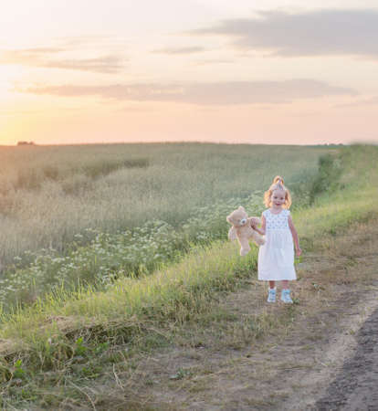 little girl with teddy bear on road at sunsetの写真素材