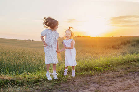 two little girl jumping in field at sunsetの写真素材