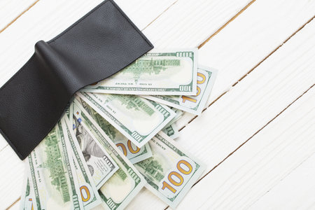 dollars in black wallet on white wooden background