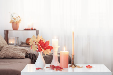 burning candles with autumn decor on white table at homeの写真素材