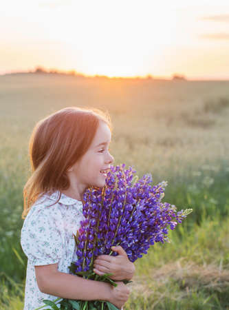 beautiful little girl with bouquet of flowers at sunsetの写真素材