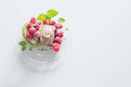 chocolate roll with raspberries and mint leaves on glass plate on white tableの写真素材