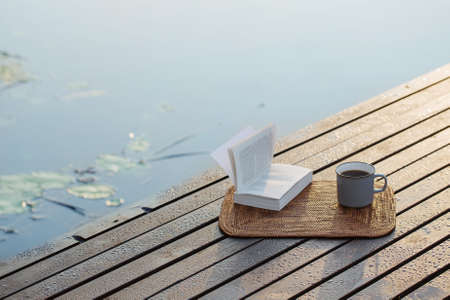 cup of coffee and book on wooden pier on summer lakeの写真素材