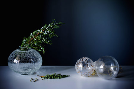 juniper branches in glass vase and christmas balls on dark blue background