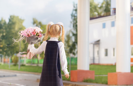 little schoolgirl with bouquet go to school in sunny day