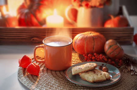 orange cup of tea and autumn decor with pumpkins, flowers and burning candles on tableの写真素材