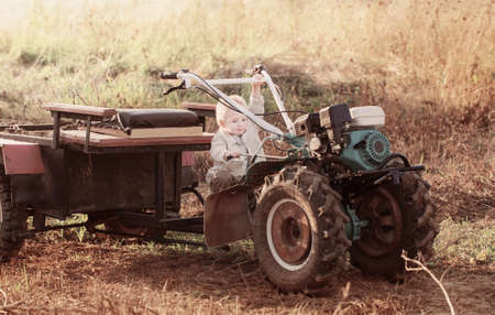 funny little boy on walk-behind tractor in fieldの写真素材