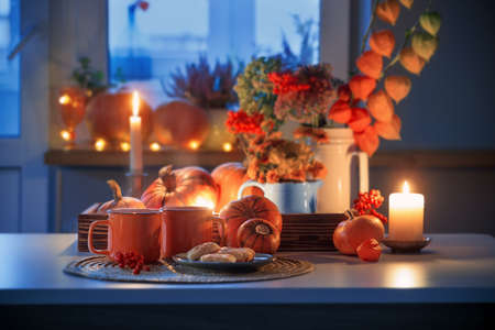 two orange cups of tea and autumn decor with pumpkins, flowers and burning candles on tableの写真素材