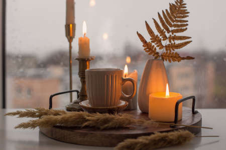 autumn still life with burning candles and a cup of coffee on the background of a window with raindropsの写真素材