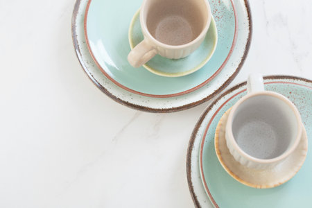 two ceramic cups and plates on white marble table