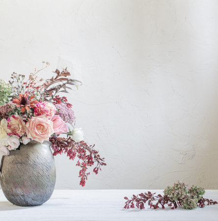 autumn flowers and berries in rustic ceramic jug on background white wall