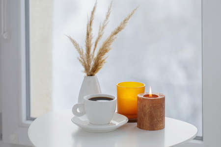 cup of coffee with burning candles on white table by window on winterの写真素材