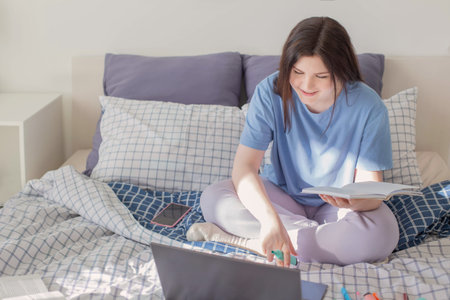 teen girl studying at home on bed with laptop