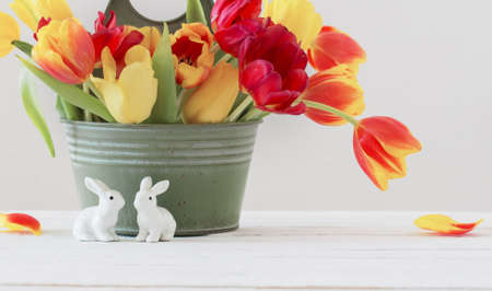 red and yellow tulips in bucket and ceramic rabbit on white backgroundの写真素材