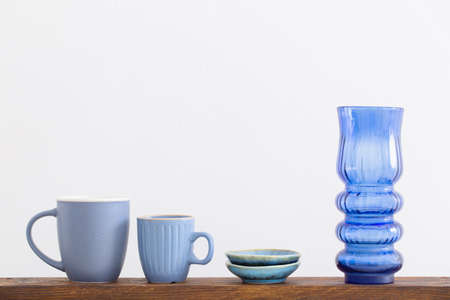 blue cups and glass vase on wooden shelf on white backgroundの写真素材