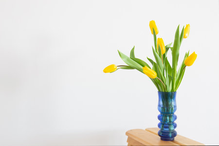 yellow tulips in blue glass vase on white backgroundの写真素材