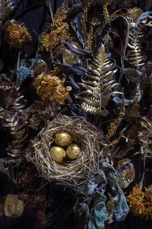 golden quail eggs in nest with dried flowers on dark wooden background