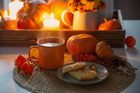 orange cup of tea and autumn decor with pumpkins, flowers and burning candles on tableの写真素材