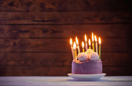 purple birthday cake with burning candles on dark wooden backgroundの写真素材