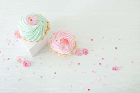 pink and green cupcakes with spring flowers on wooden podiums on white backgroundの写真素材
