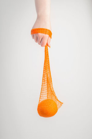 female hand with orange and synthetic string bag