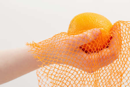 female hand with orange and synthetic string bagの写真素材