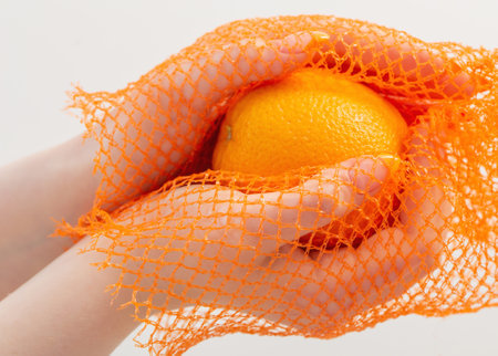 female hand with orange and synthetic string bagの写真素材