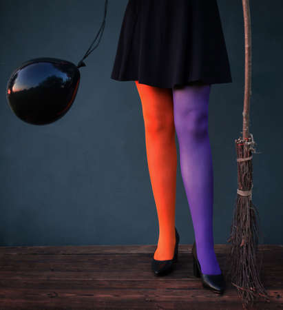 witch legs in multicolored tights with black balloon and broom on blue backgroundの写真素材