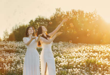 two young beautiful girls on meadow with dandelions at sunsetの写真素材
