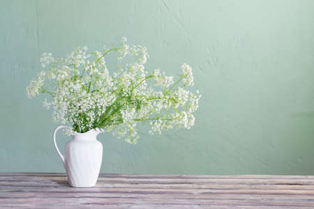 white wild flowers in jug on background green wallの写真素材