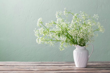 white wild flowers in jug on background green wallの写真素材
