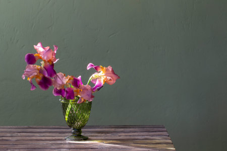irises in beautiful glass vase against green wall