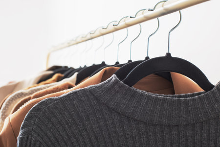 female autumn clothes on hangers in white room close up