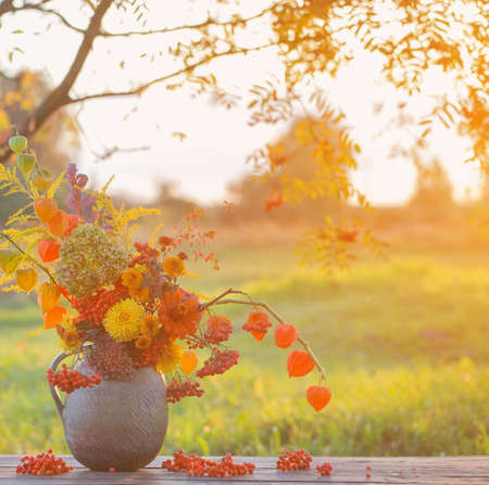 bouquet autumn flowers in rustic jug on wooden table outdoor at sunsetの写真素材