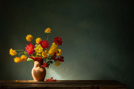 red and yellow flowers on jug in sunlight on background dark wallの写真素材