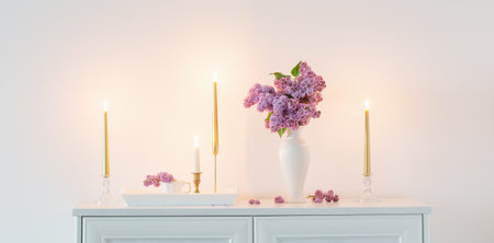 lilac flowers in white vase and golden candles on background white wallの写真素材