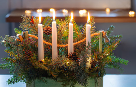 advent decoration with fir branches and four burning candles in wooden basket on white table at homeの写真素材