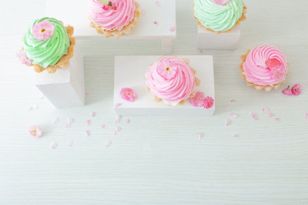 pink and green cupcakes with spring flowers on wooden podiums on white background