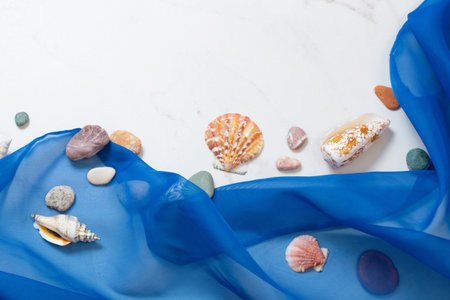 sea background with blue cloth, stones, seashells on white marbleの写真素材