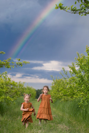 two girls running in summer garden with rainbowの写真素材