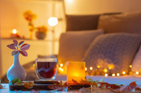 thermo glass with hot tea in dark night room with autumnal leavesの写真素材