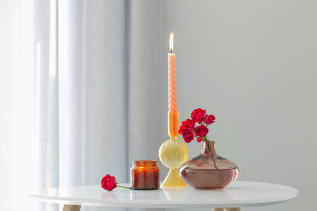 red roses in vase with burning candles in white interiorの写真素材