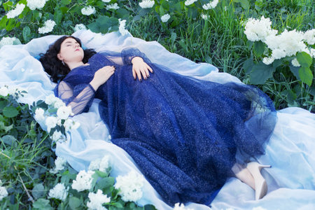 young beautiful woman in blue dress on grass with white flowersの写真素材