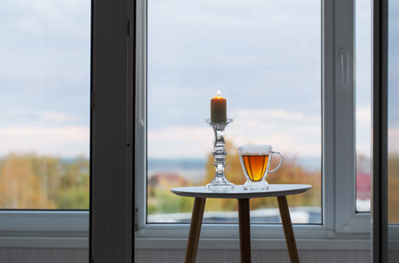 glass thermo cup with tea and burning candles on background window with autumnal landscapeの写真素材