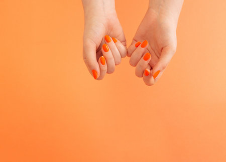 female hands with orange manicure on orange backgroundの写真素材