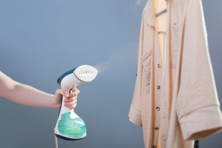 female hand with steamer and shirt on blue backgroundの写真素材