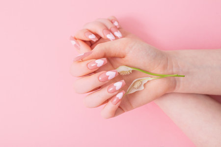 female hands with beautiful long nails with flowers on pink backgroundの写真素材