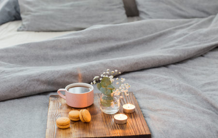 cup of tea with macaroons and candles on wooden tray on bed