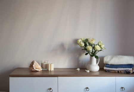 knitted clothing and white roses in jug on modern dresser