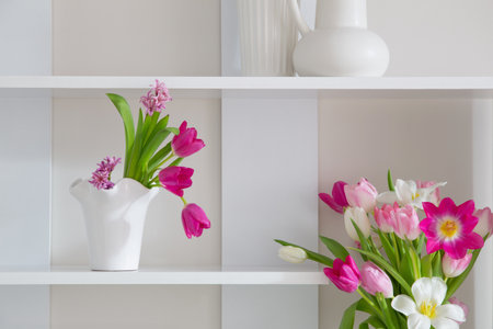 white and pink tulips in vases on white shelfの写真素材